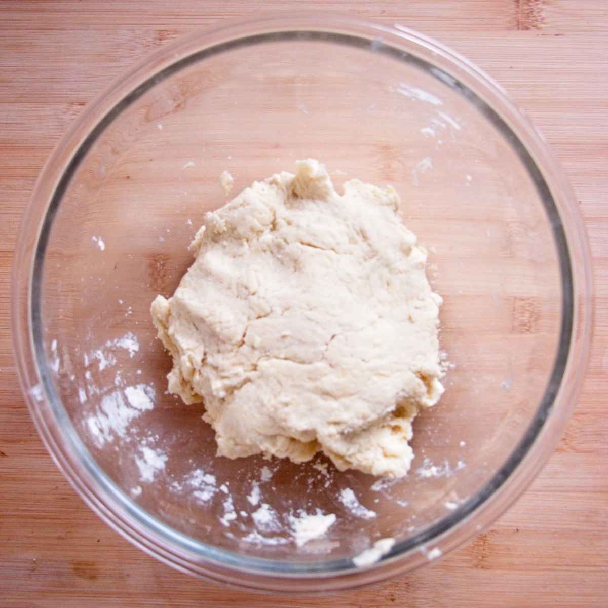 Soft scone dough formed in a glass mixing bowl on a wooden surface