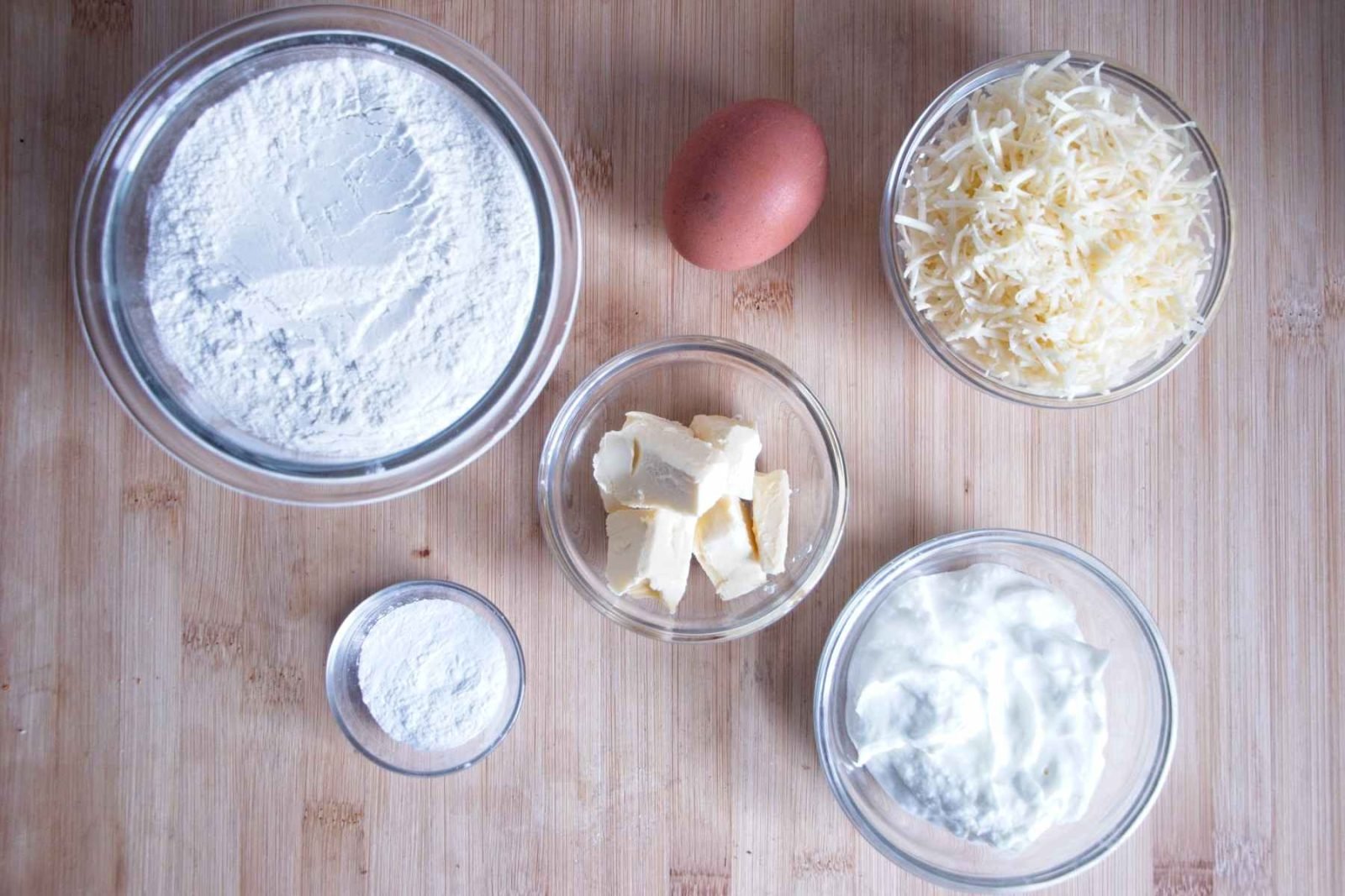 Ingredients for high protein scones laid out on a wooden board, including flour, butter, egg, skyr, and grated cheese