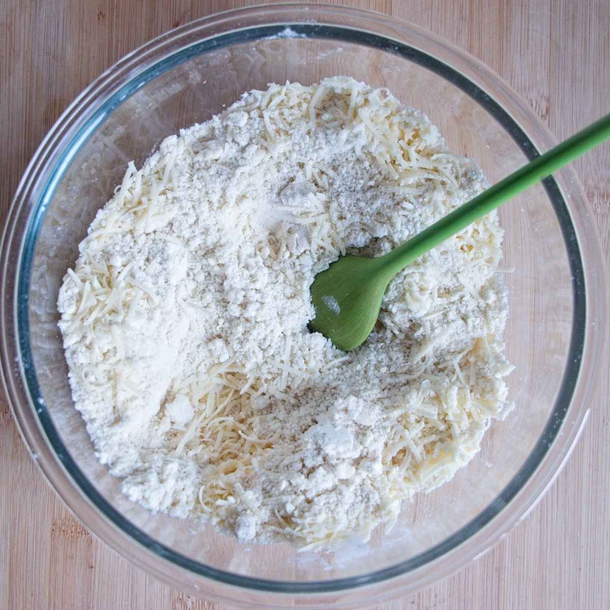Flour and grated cheese mixed together in a glass bowl with a spatula