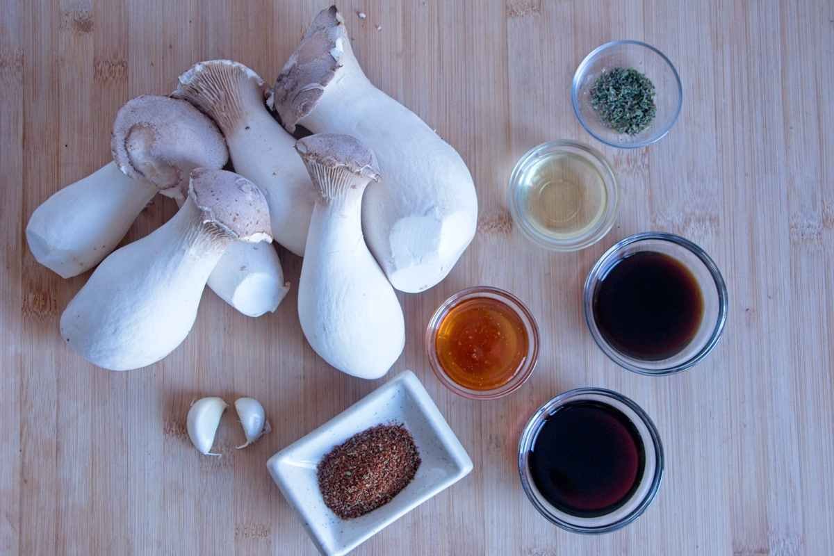 Mushroom jerky ingredients laid out on a wooden board, including king oyster mushrooms, soy sauce, vinegar, spices, garlic, and sweetener.