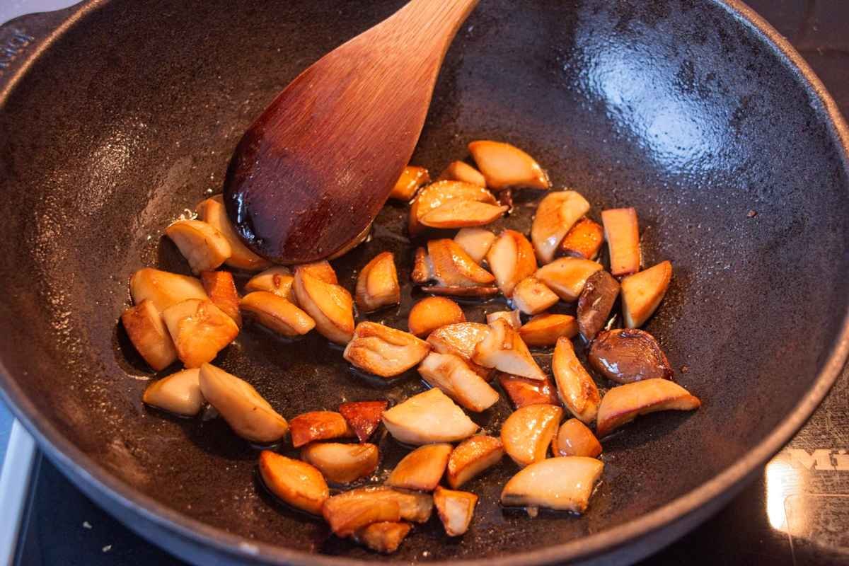 King oyster mushroom pieces browning in a hot pan with a wooden spoon