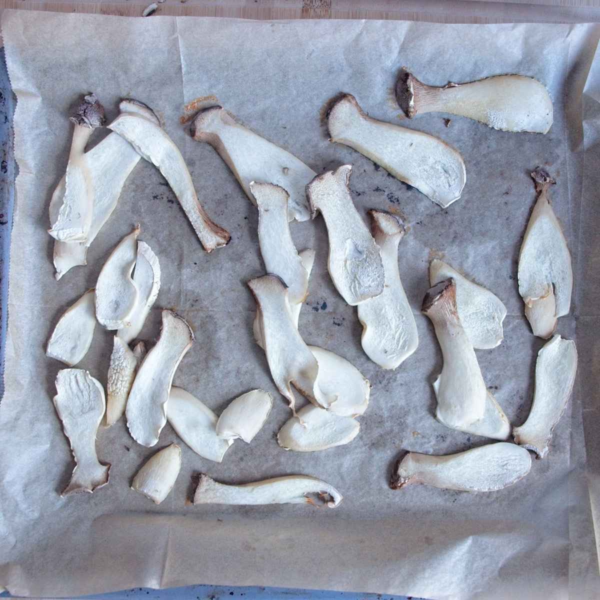 Par-cooked king oyster mushroom slices laid out on a lined baking tray after softening, ready to be marinated before drying.