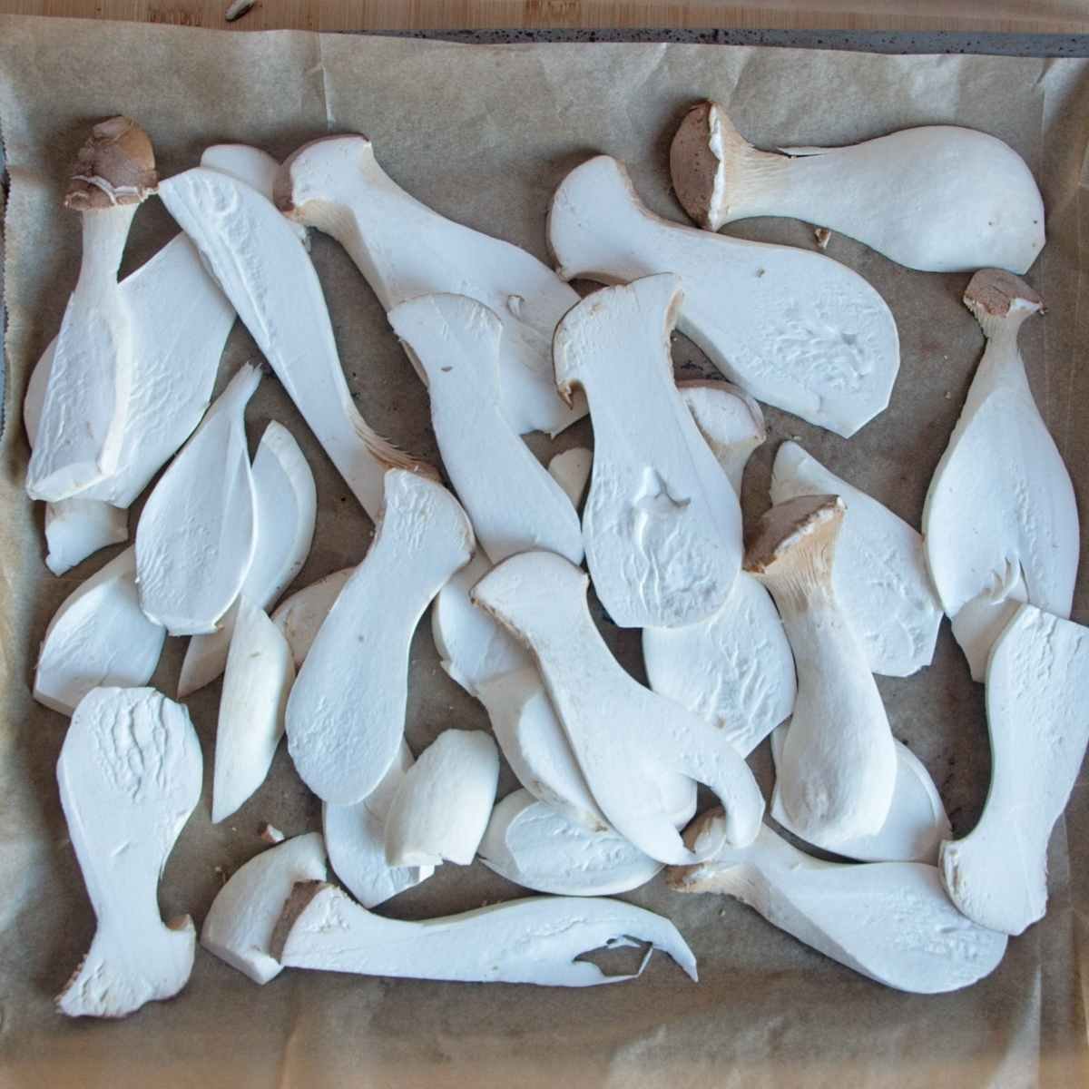 Raw king oyster mushrooms sliced lengthways and arranged on a lined baking tray before par-cooking or marinating.