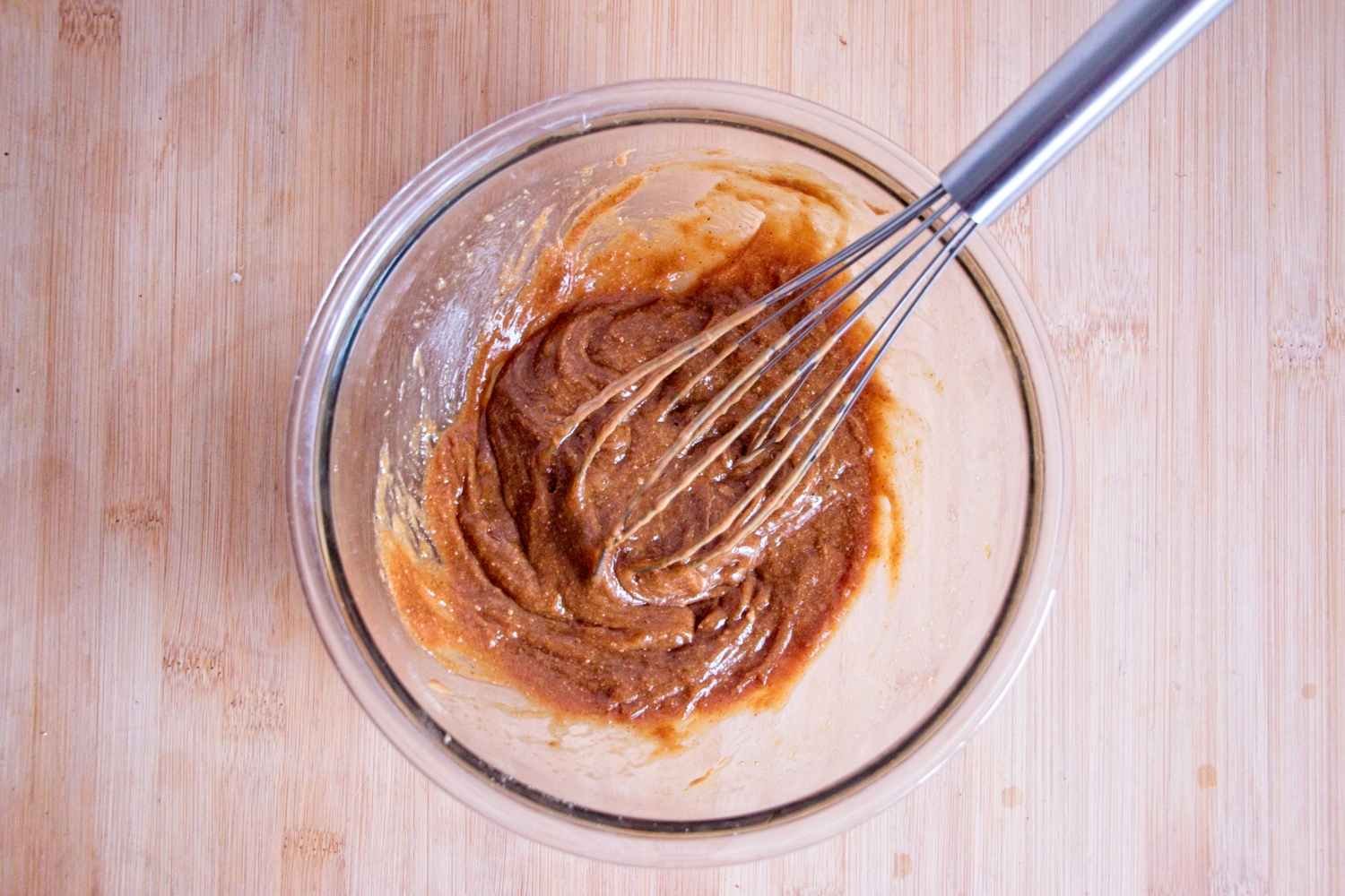 Peanut butter and sugar mixture being whisked in a glass bowl on a wooden surface