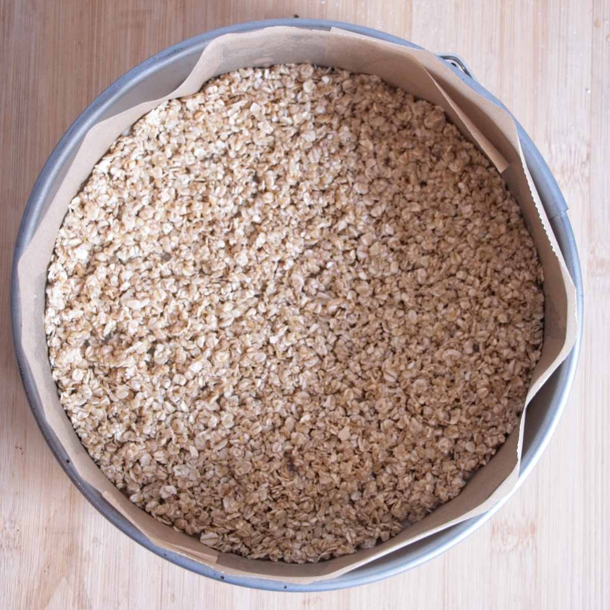 Oat cheesecake base pressed evenly into a lined cake tin before baking
