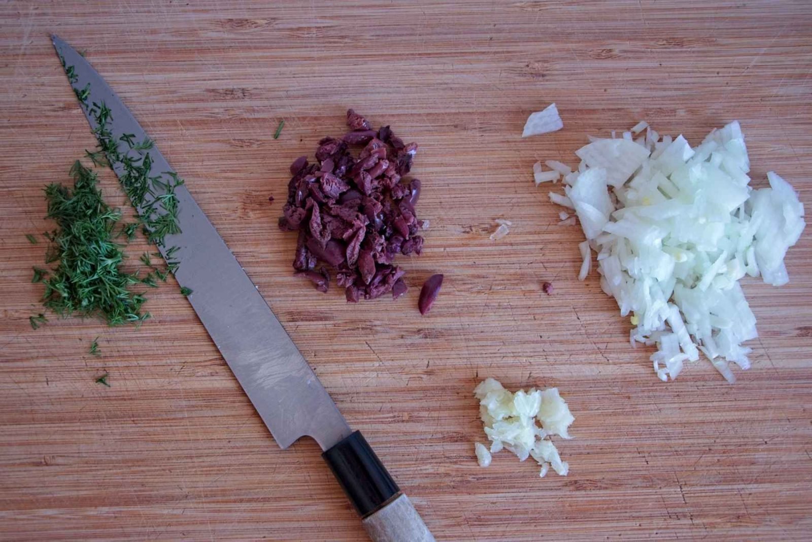 Chopped onion, garlic, dill and olives prepared on a wooden board