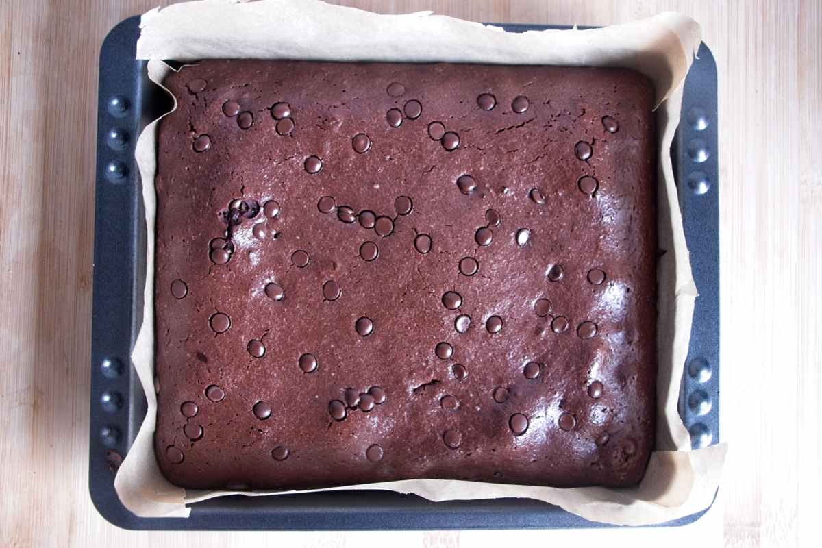 Baked protein brownies in a lined tin with a set, glossy chocolate surface.