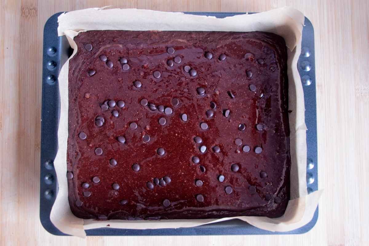 Chocolate brownie batter spread in a lined baking tin before baking.