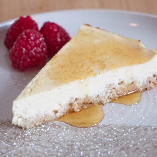 Protein cheesecake without protein powder showing a close-up of the creamy filling, oat base, honey drizzle, and fresh raspberries