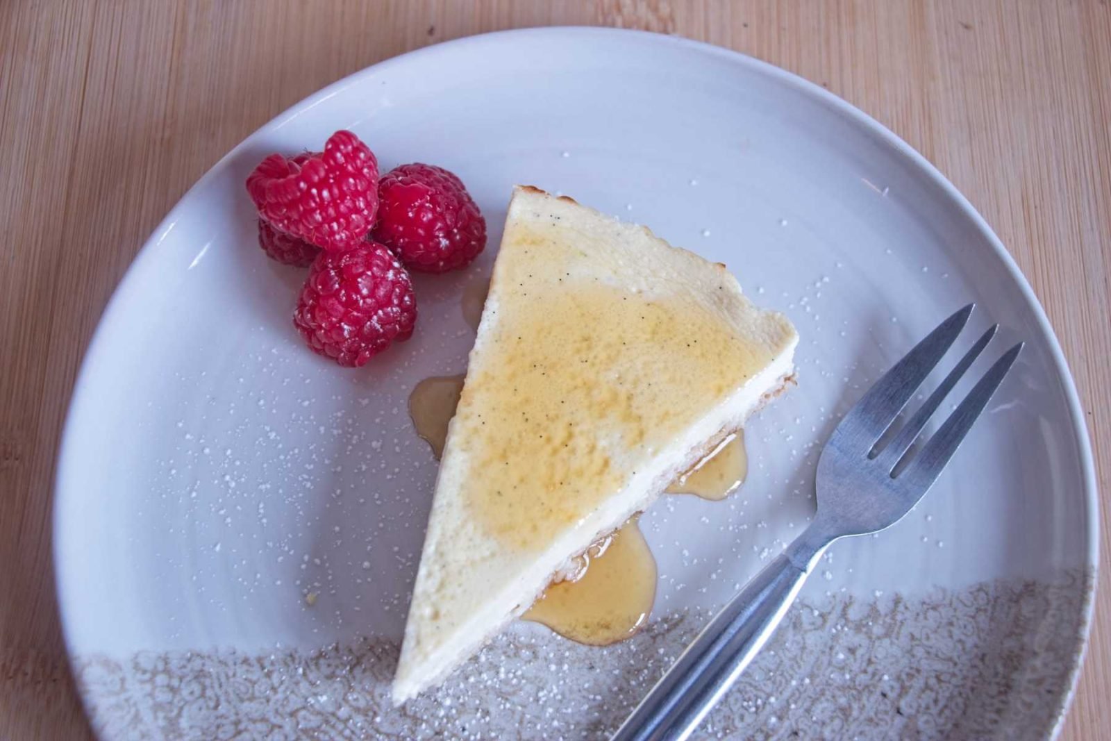 Protein cheesecake without protein powder served as a slice on a plate with honey drizzle and fresh raspberries
