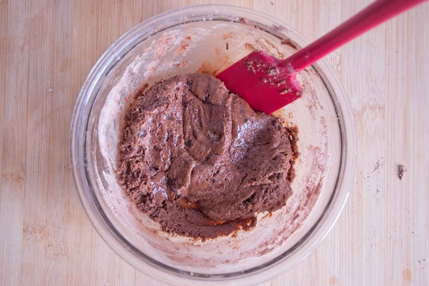 Chocolate cookie dough mixed in a glass bowl with a spatula, ready to bake