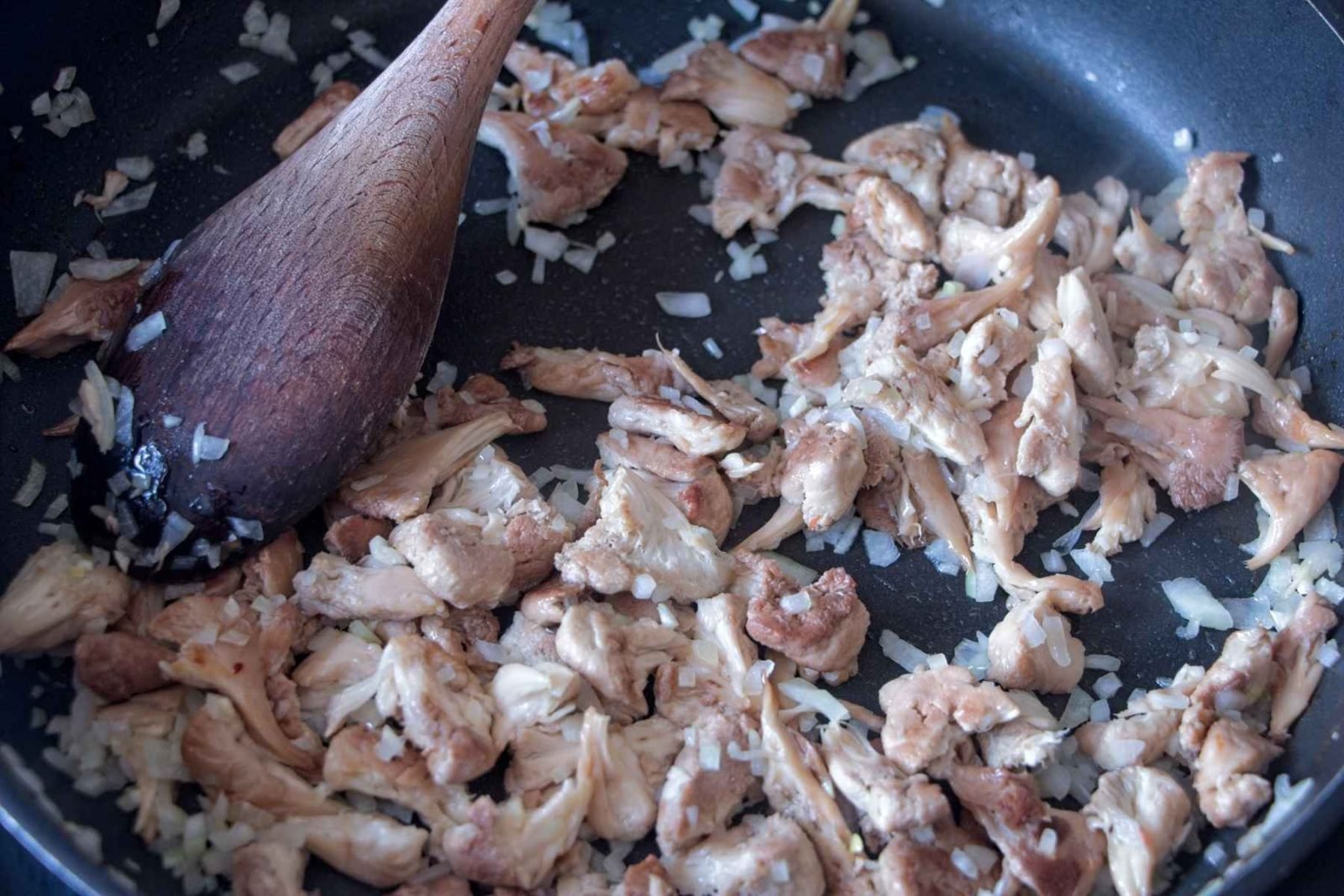 Shredded mushrooms cooking in a pan with onion as the base softens and browns