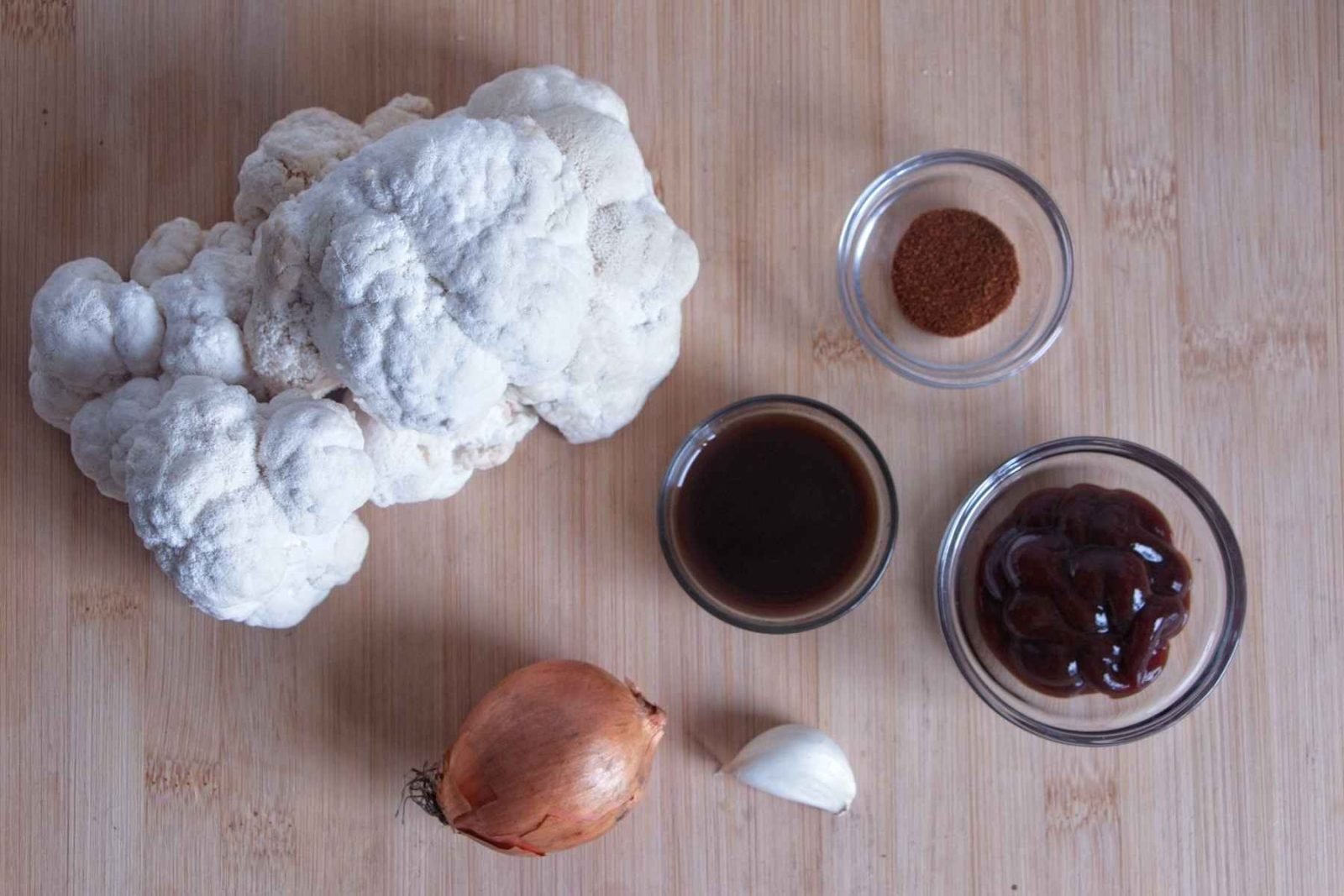 Ingredients for pulled lion’s mane mushroom laid out on a board, including fresh lion’s mane, onion, garlic, BBQ sauce, soy sauce, and smoked paprika