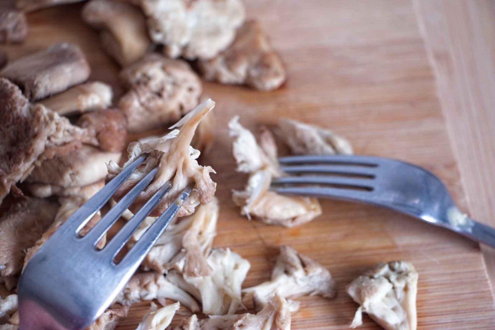 Pulled lion’s mane mushroom being shredded with forks on a chopping board