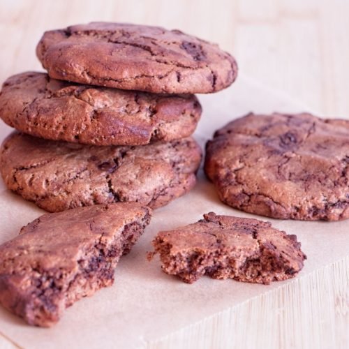 Chocolate peanut butter protein cookies stacked on parchment with a broken cookie showing the soft centre