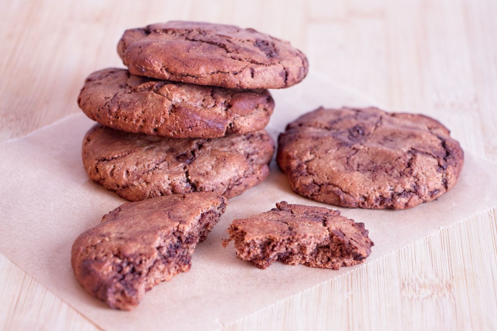 Chocolate peanut butter protein cookies stacked on parchment with a broken cookie showing the soft centre