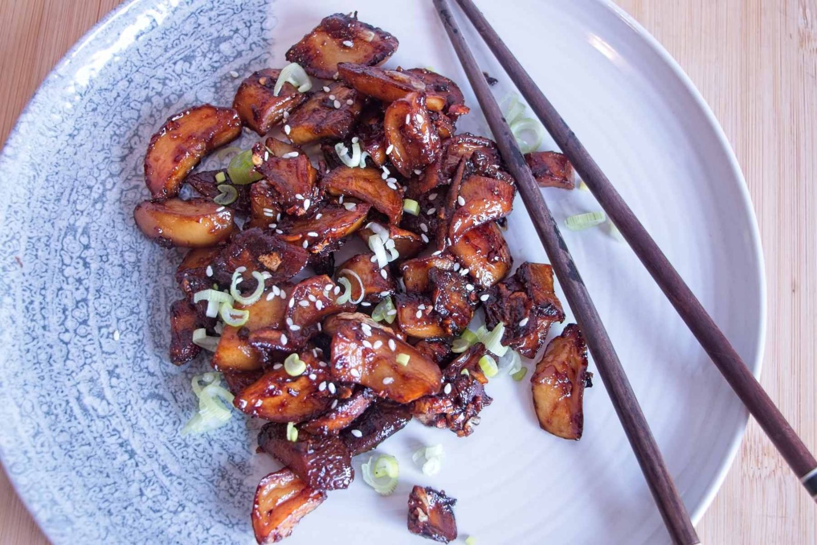 Sticky king oyster mushrooms served on a plate with a garlic soy miso glaze, topped with spring onions and sesame seeds