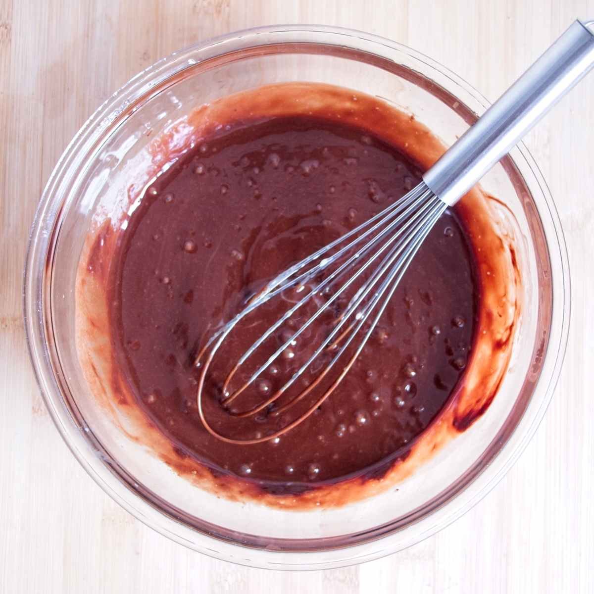 Chocolate brownie batter whisked smooth in a glass bowl.