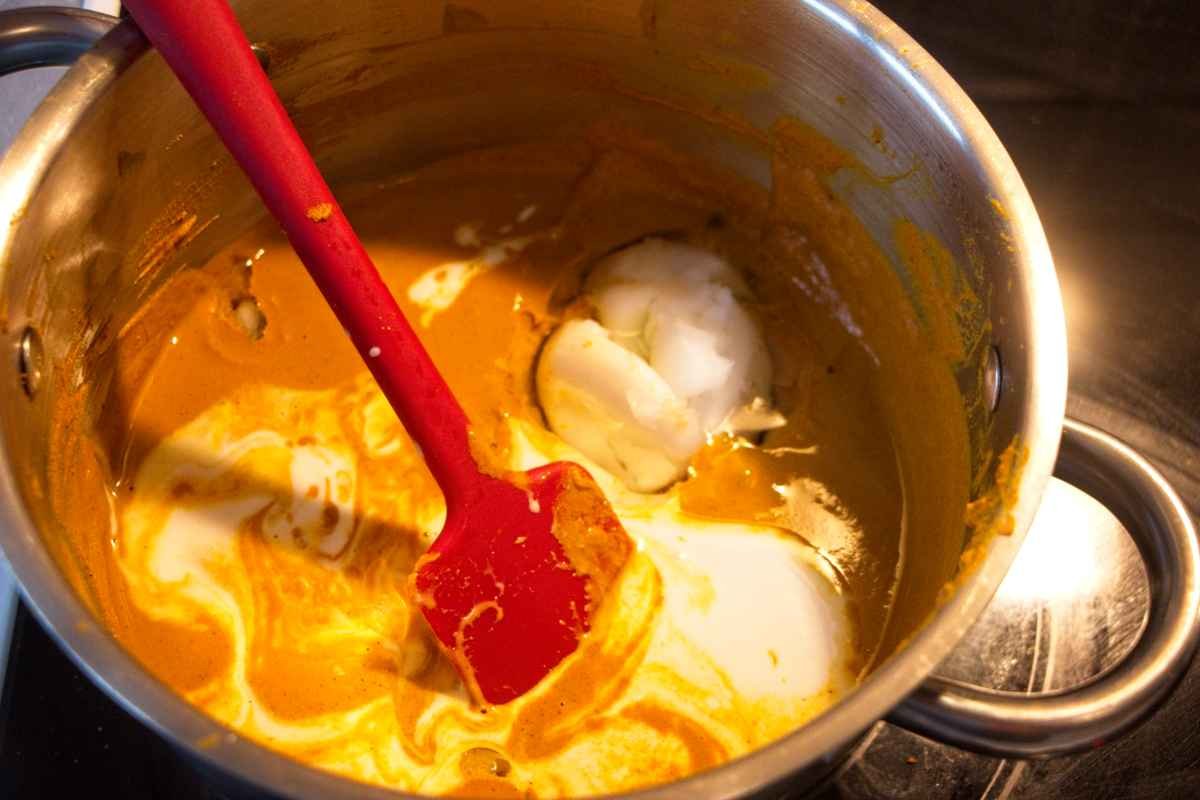 Coconut milk and oil being stirred into the turmeric mixture in a saucepan to enrich the paste before blending.