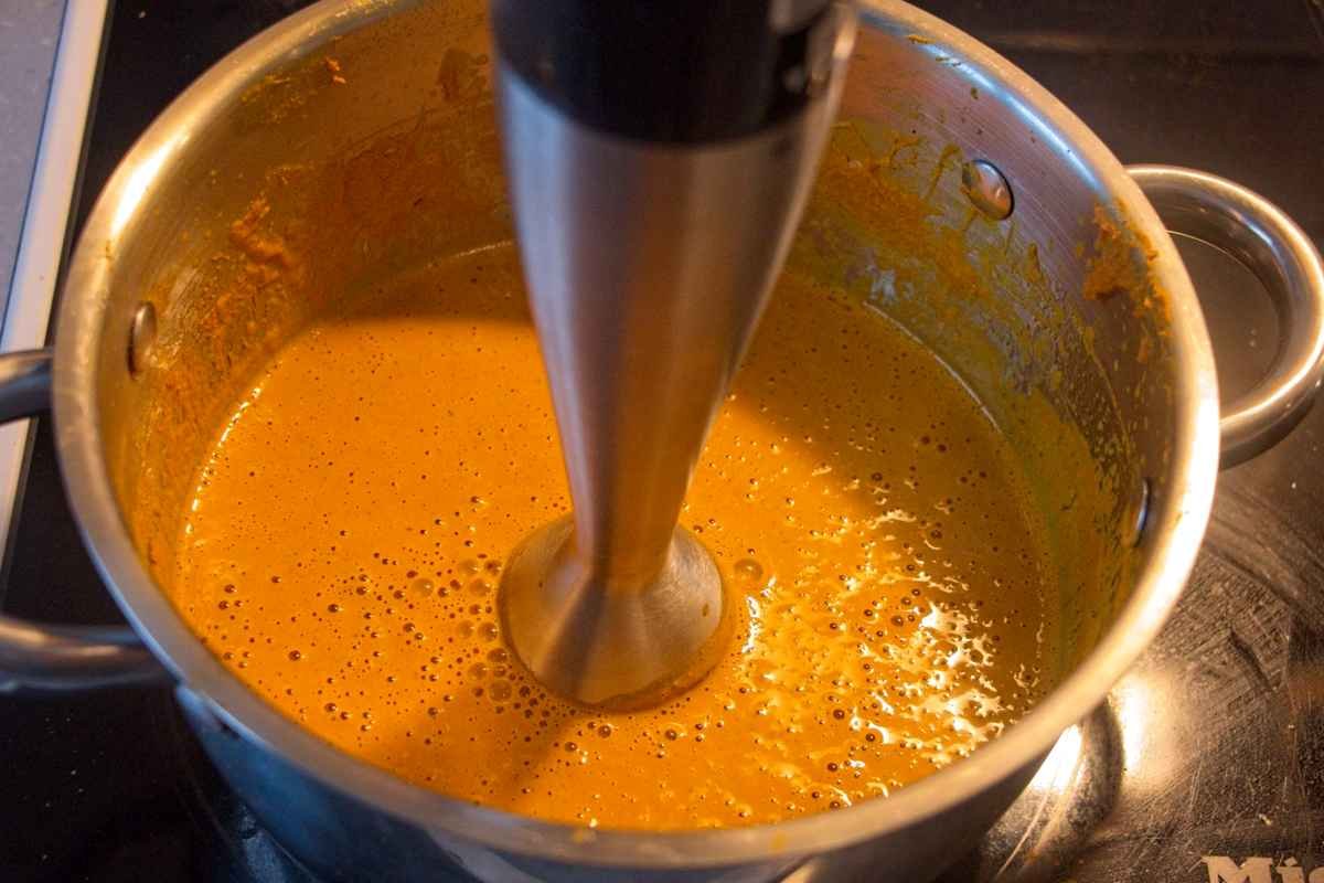 Blending golden milk concentrate in a saucepan with a stick blender until smooth and emulsified.