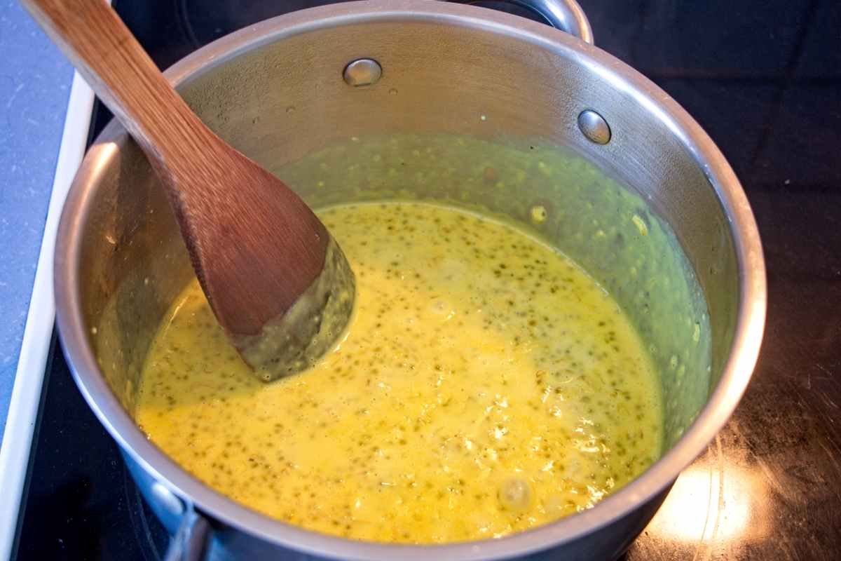 Turmeric oatmeal cooking in a saucepan on the hob, stirred with a wooden spoon until creamy.