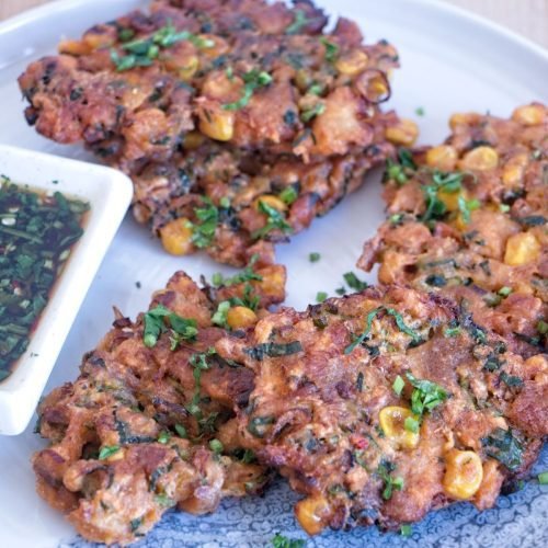 Crispy lion’s mane mushroom fritters served on a plate with chopped herbs and visible sweetcorn, showing golden edges and a structured texture.