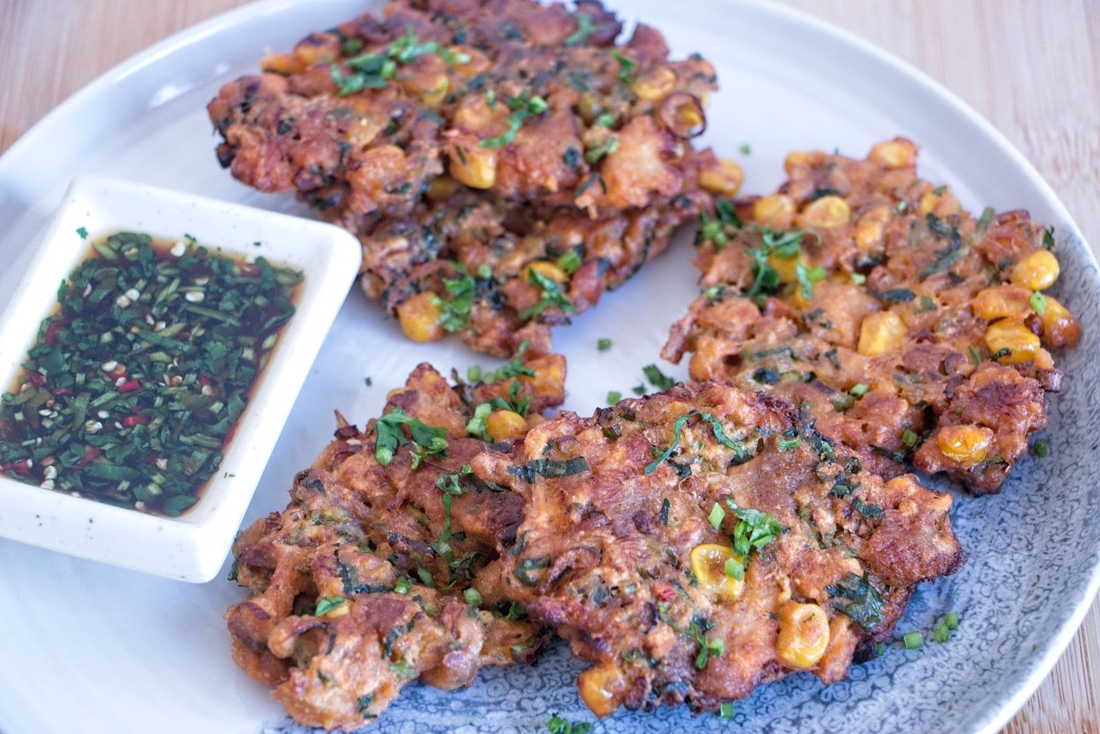 Crispy lion’s mane mushroom fritters served on a plate with chopped herbs and visible sweetcorn, showing golden edges and a structured texture.