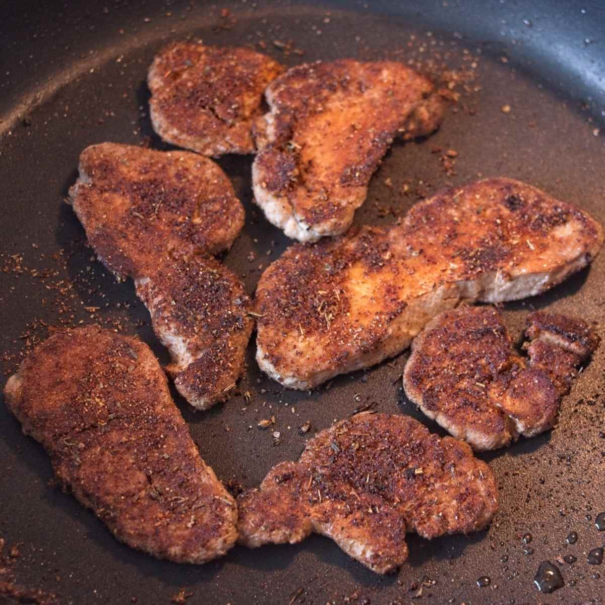 Deeply browned mushroom pieces cooking in a pan with crisp edges and seasoning