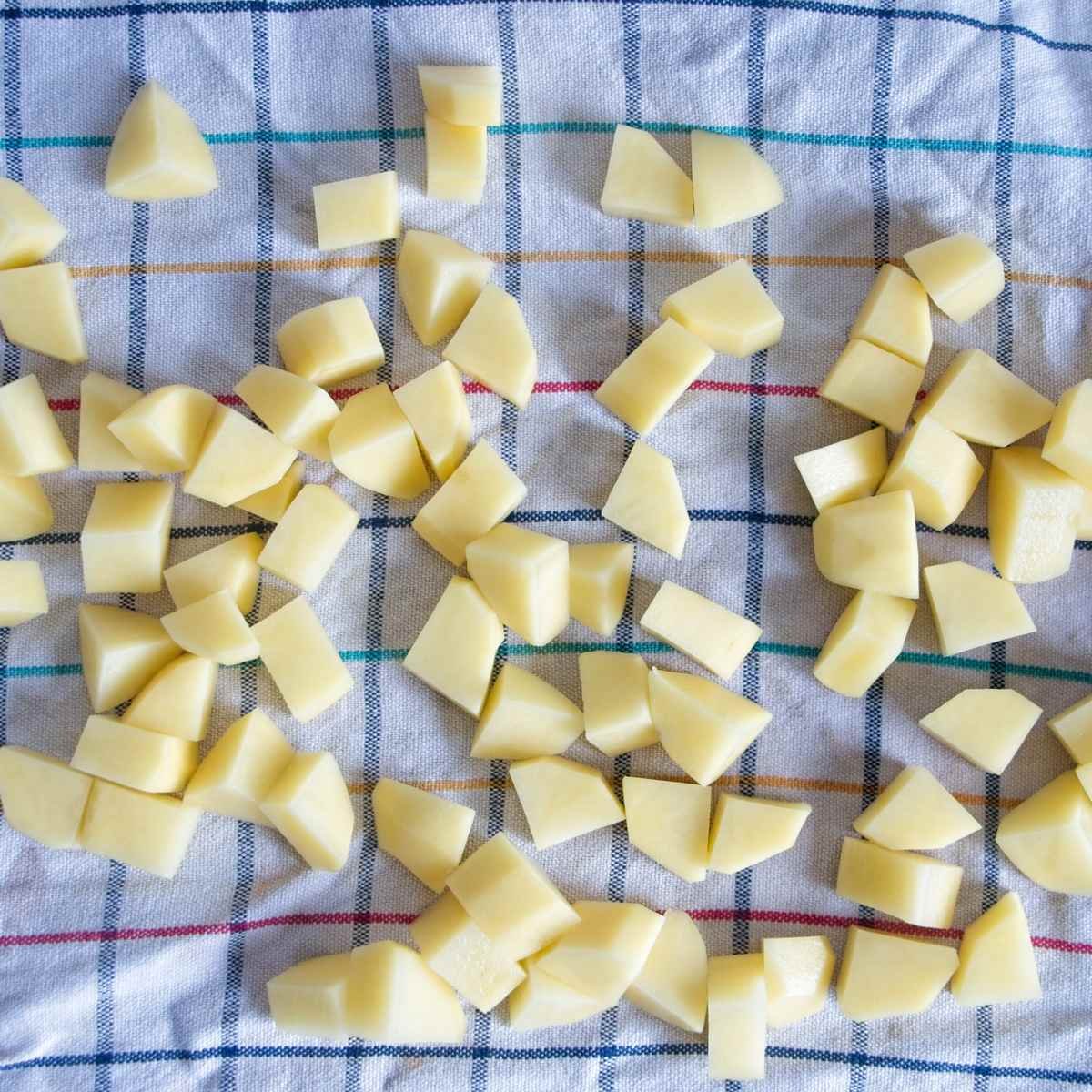 Diced potatoes spread on a kitchen towel to dry before cooking.