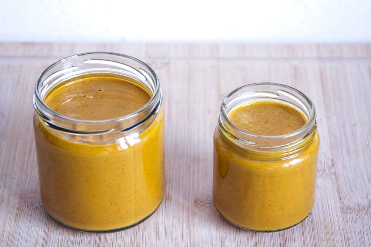 Two jars filled with golden milk concentrate paste on a wooden surface, showing the thick spoonable texture.