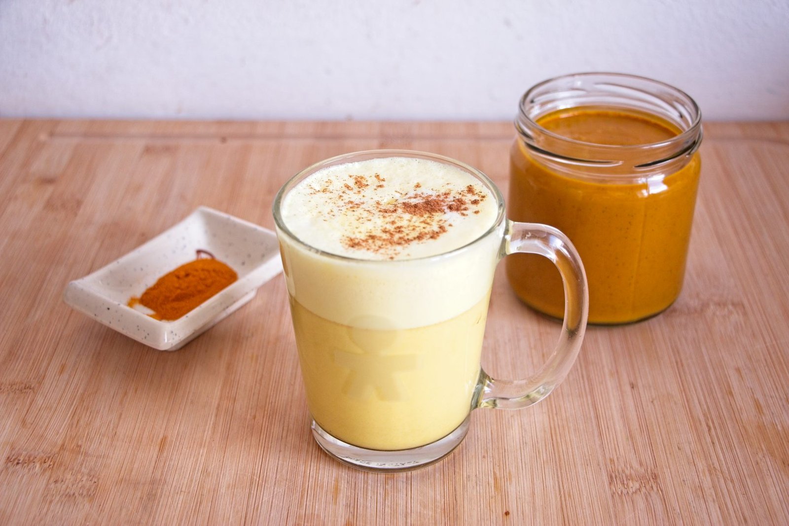 Glass mug of golden milk made with golden milk concentrate, topped with light foam and cinnamon, with a jar of concentrate in the background.