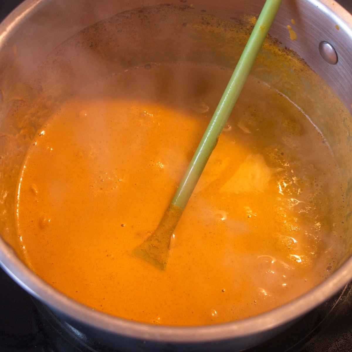 Turmeric mixture gently simmering in a saucepan as it thickens and reduces to a smooth paste.