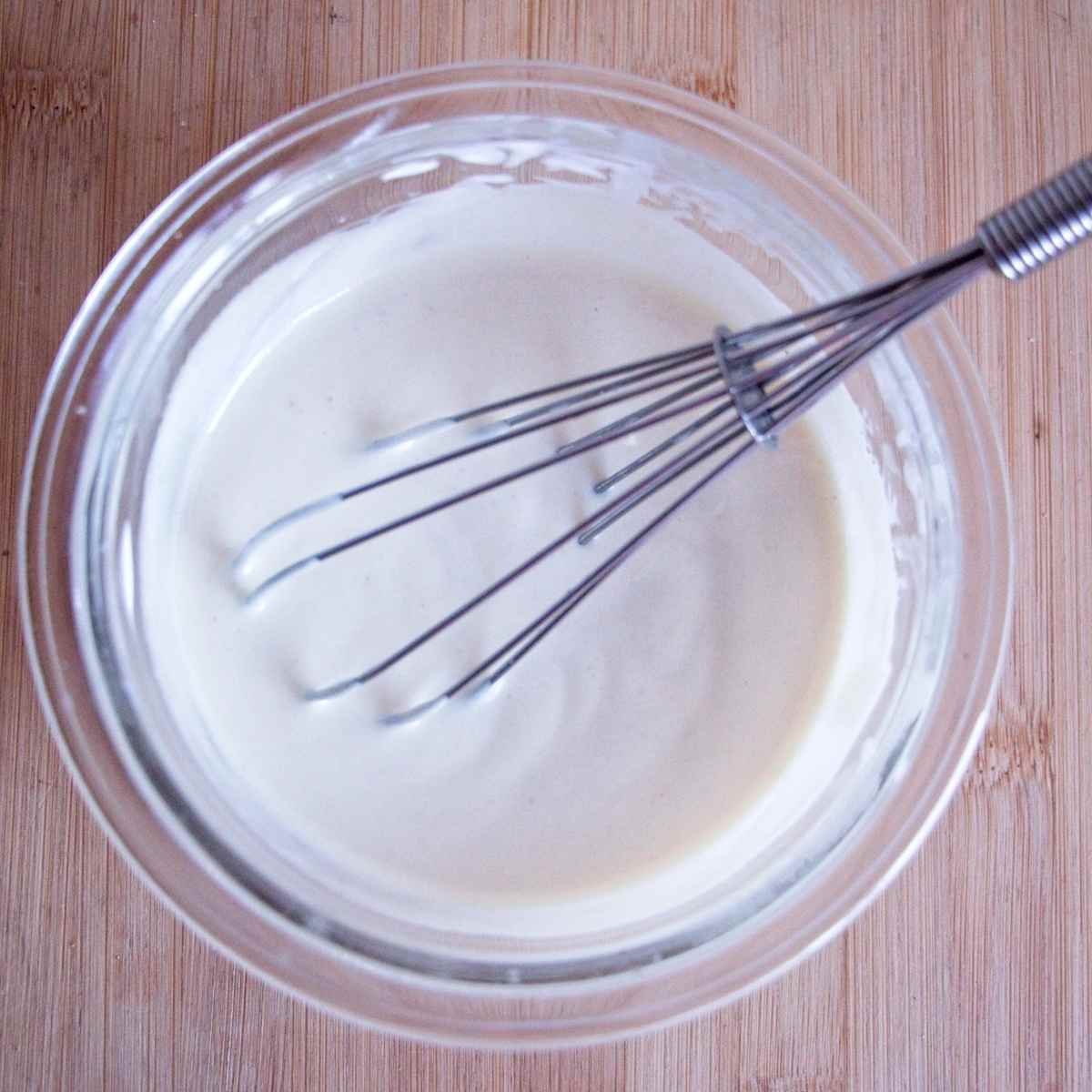 Greek yogurt dressing whisked smooth in a glass bowl.