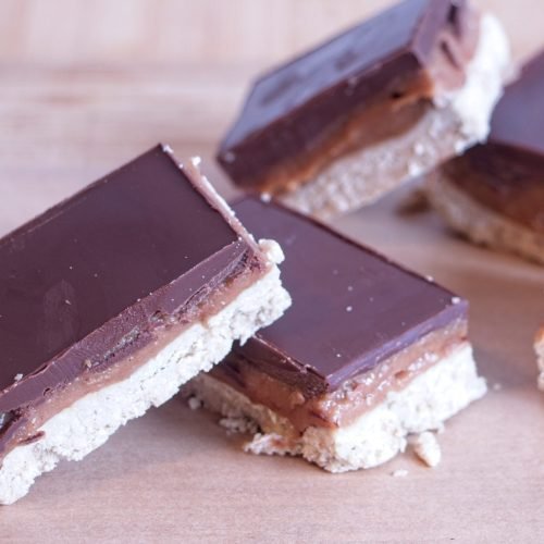 High protein millionaire’s shortbread slices arranged on baking paper, showing chocolate topping, caramel layer, and oat base