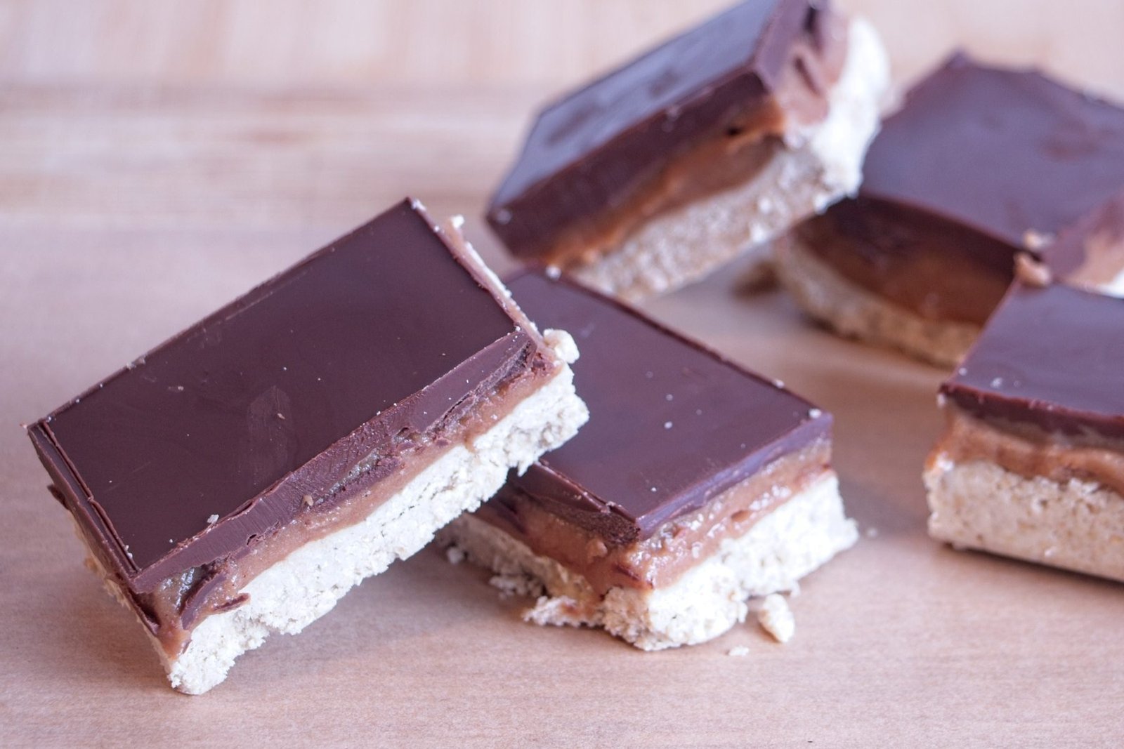 High protein millionaire’s shortbread slices arranged on baking paper, showing chocolate topping, caramel layer, and oat base