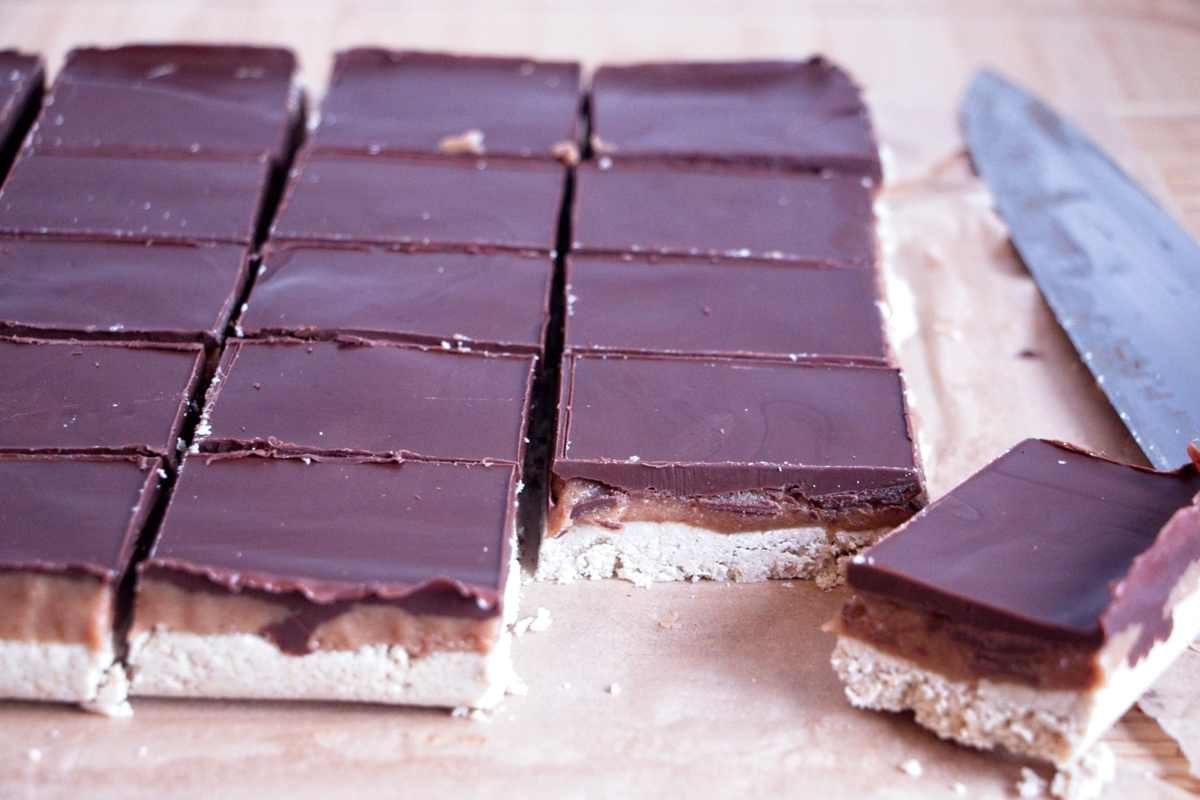 High protein millionaire’s shortbread sliced into even squares in the tray, showing chocolate, caramel, and oat base layers