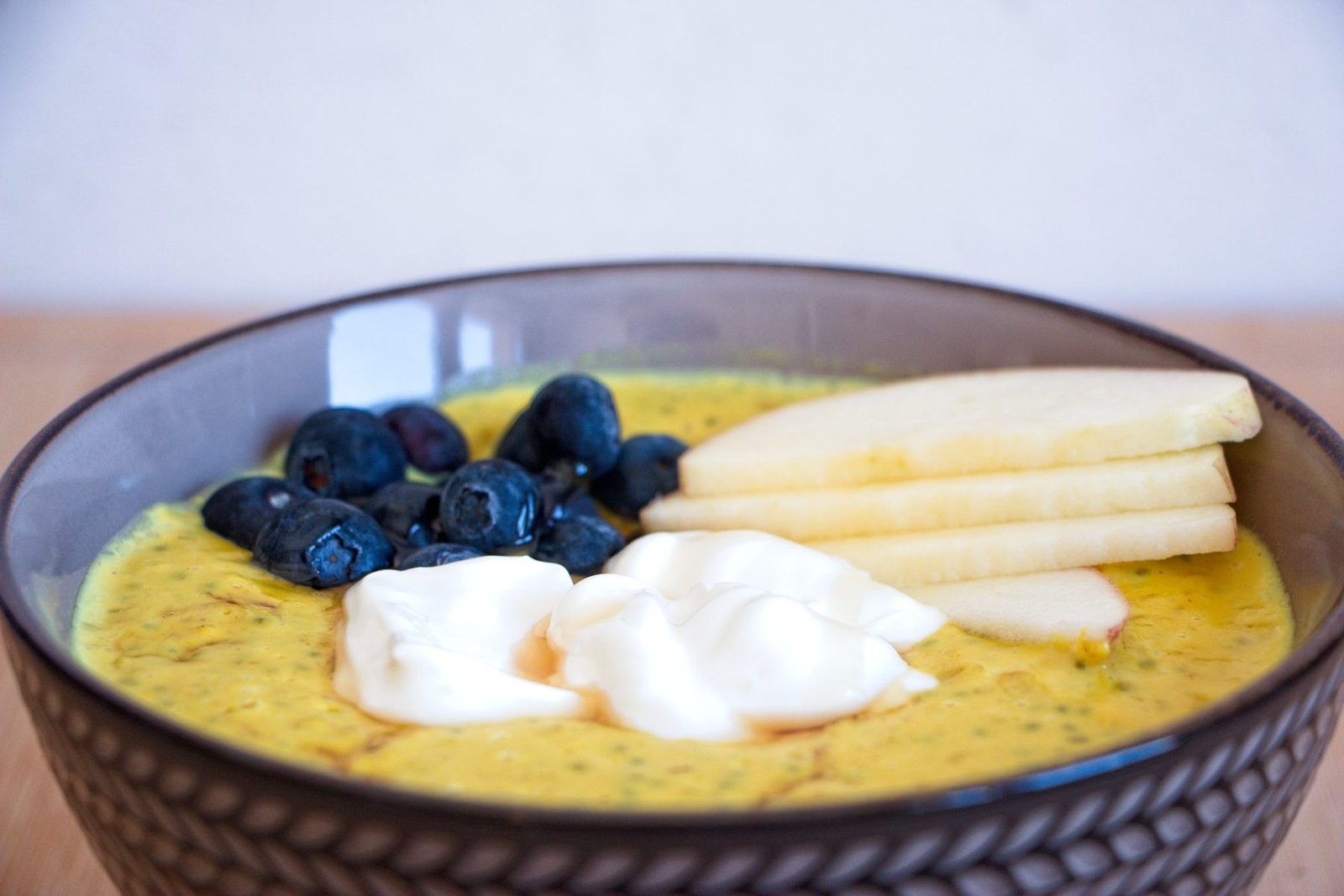High protein oatmeal in a bowl topped with blueberries, sliced apple and Greek yoghurt, photographed from the side.