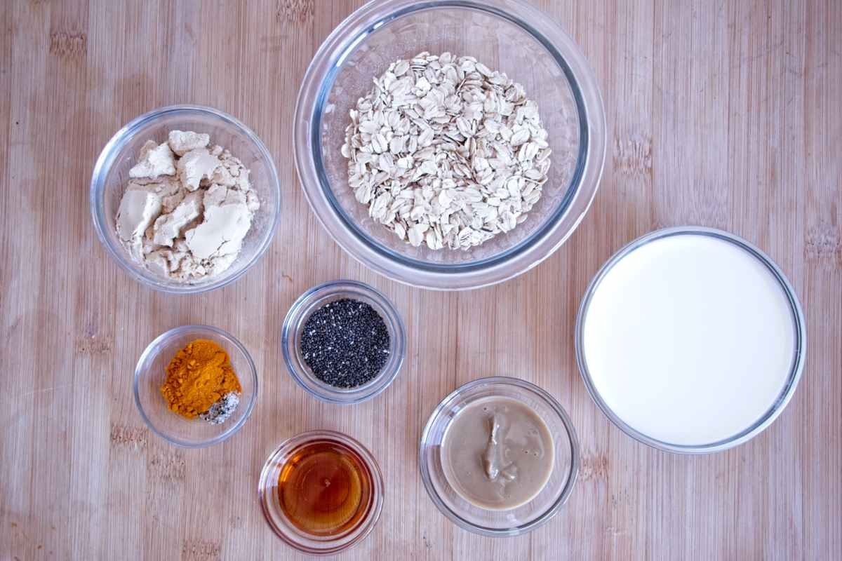 Ingredients for high protein oatmeal including rolled oats, whey protein powder, milk, chia seeds, turmeric, cashew butter and maple syrup.