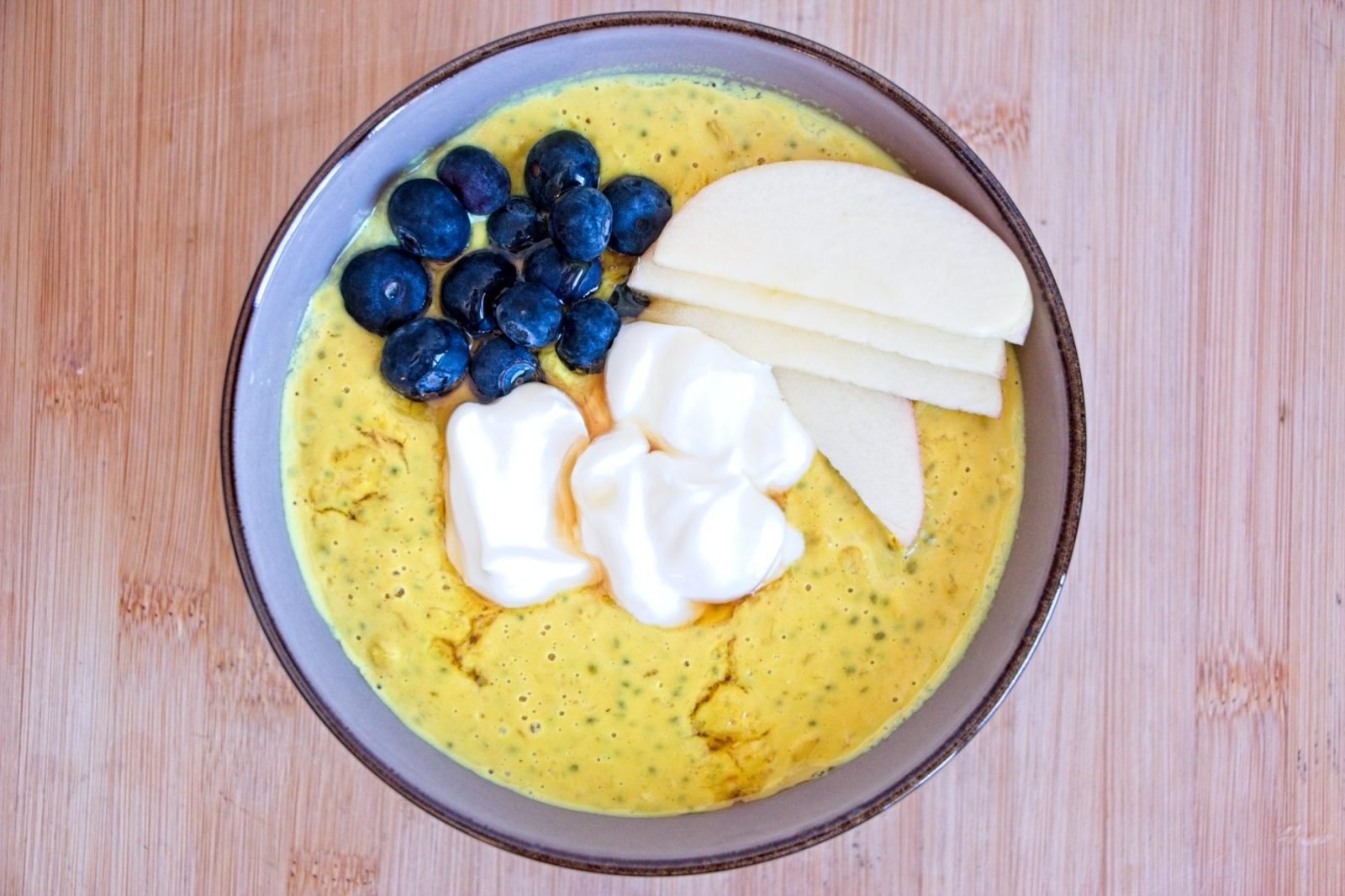 High protein oatmeal topped with blueberries, sliced apple and Greek yoghurt, served in a bowl from overhead.