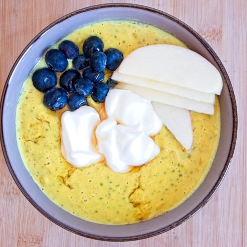 High protein oatmeal topped with blueberries, sliced apple and Greek yoghurt, served in a bowl from overhead.