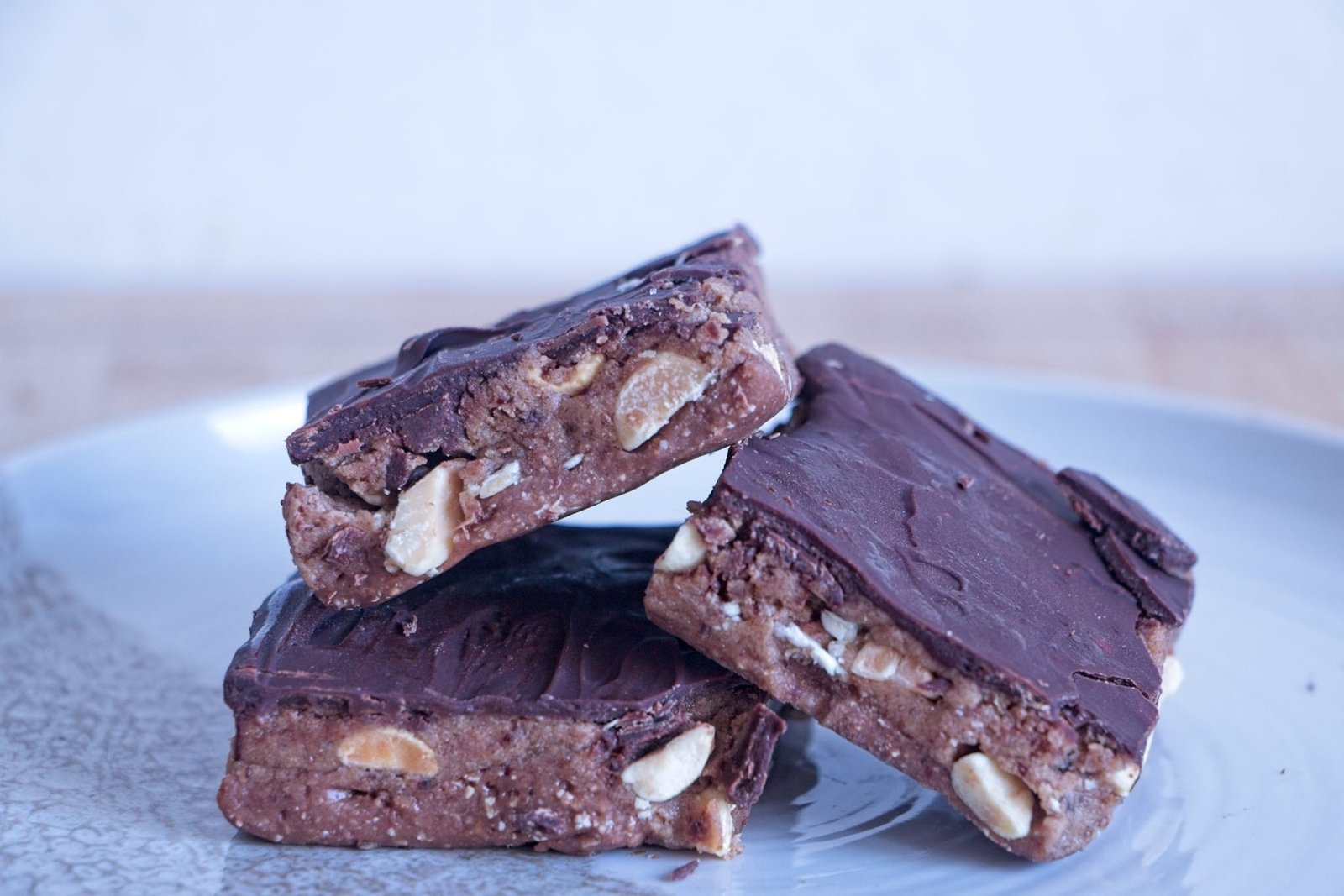 Stack of High-Protein Snickers Bites on a plate, showing the peanut nougat, date caramel, roasted peanuts, and dark chocolate top layer.