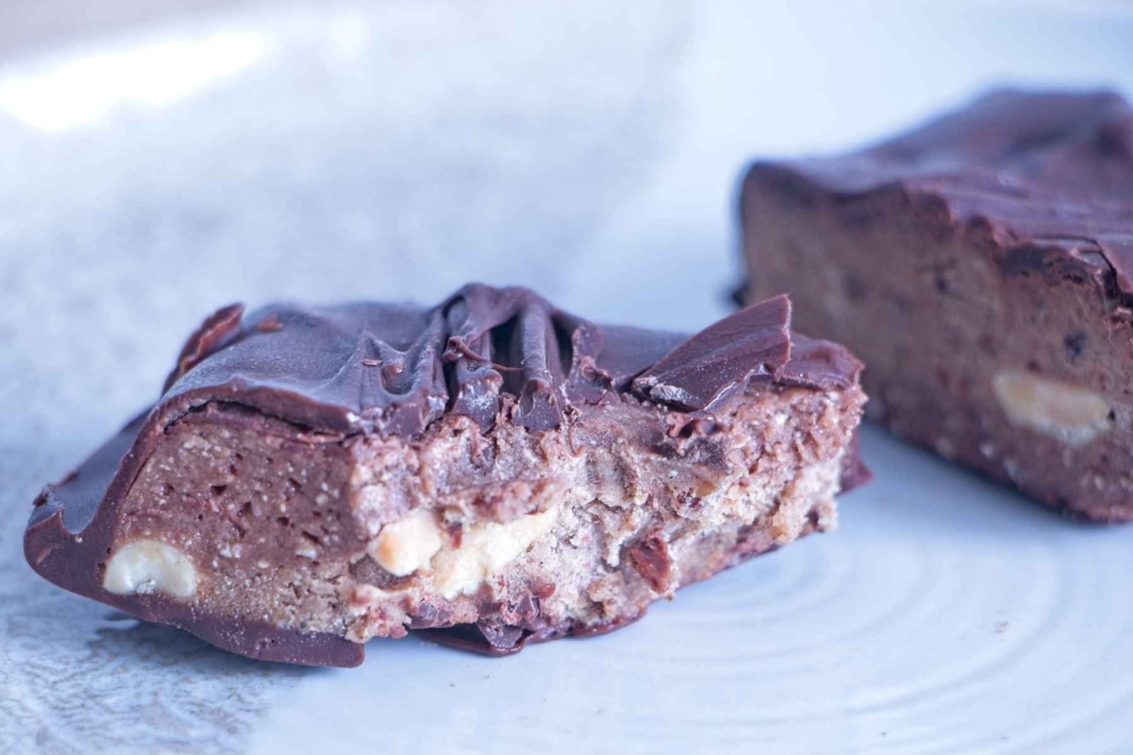 Close-up of High-Protein Snickers Bites showing the peanut nougat, date caramel, roasted peanuts, and dark chocolate top with a clean bite through the centre.