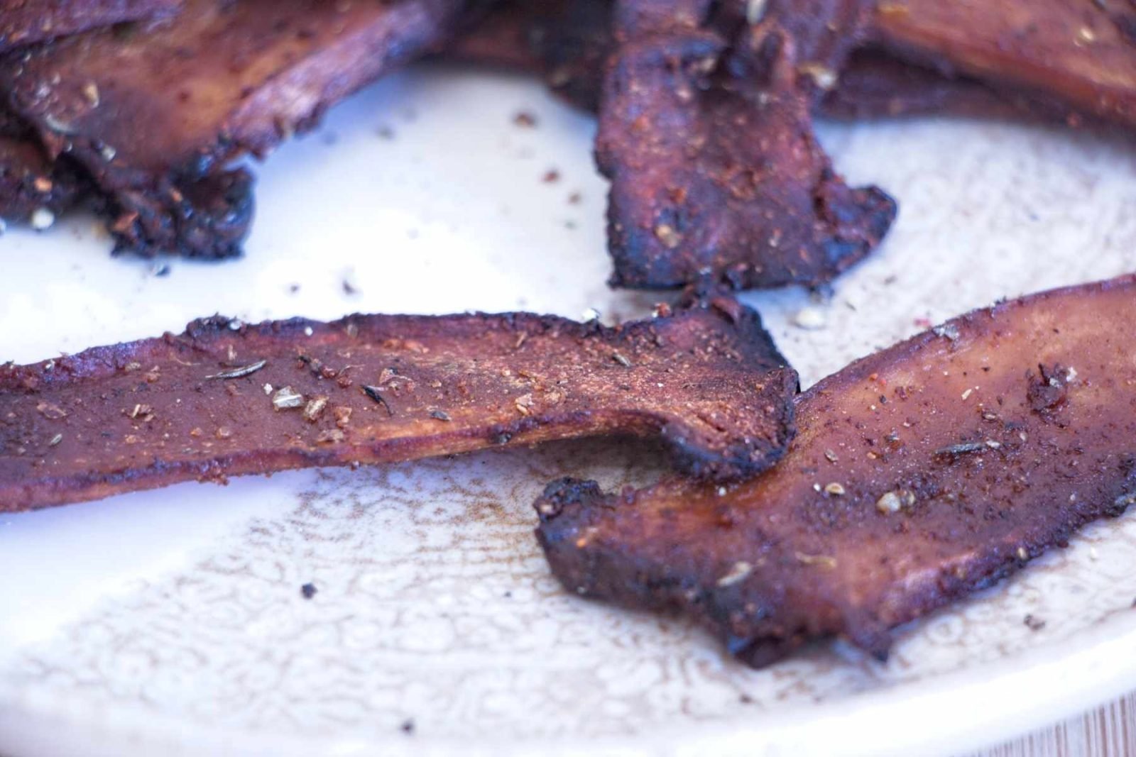 Close-up of Crispy King Oyster Mushroom Bacon showing charred edges and pepper flakes on a plate.