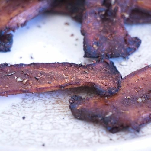 Close-up of Crispy King Oyster Mushroom Bacon showing charred edges and pepper flakes on a plate.