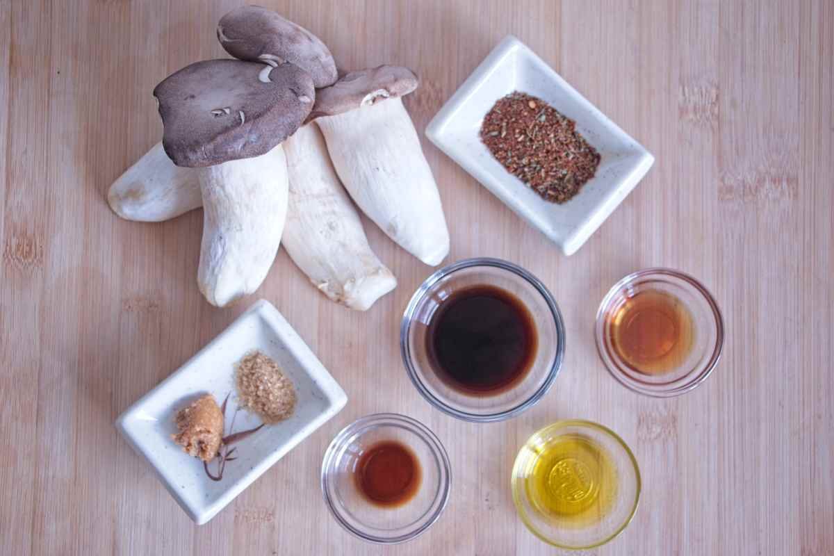 Ingredients for Crispy King Oyster Mushroom Bacon including king oyster mushrooms, soy sauce, maple syrup, olive oil, miso and spices arranged on a wooden board.