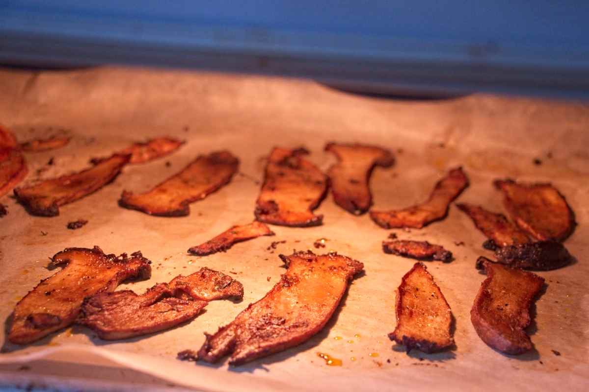 Crispy King Oyster Mushroom Bacon baking on a lined tray in the oven, edges caramelised and slightly curled.