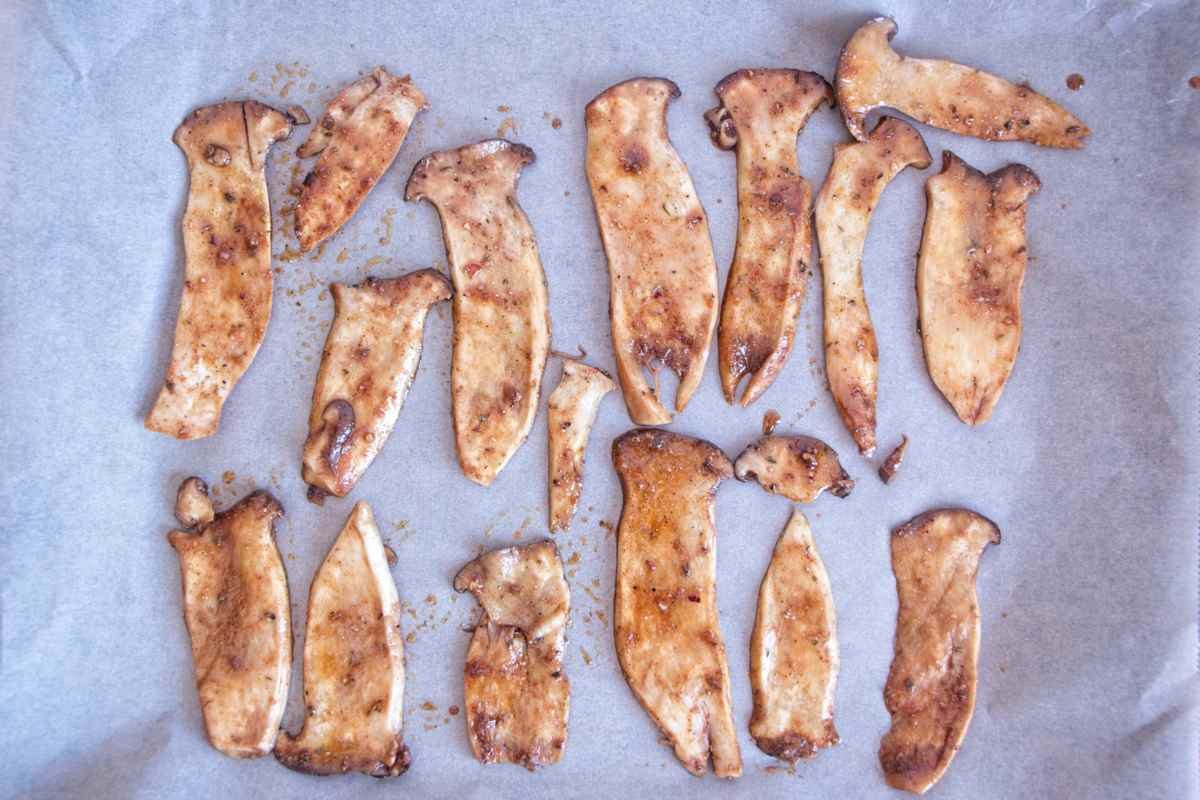 Marinated king oyster mushroom slices arranged on parchment paper before baking.