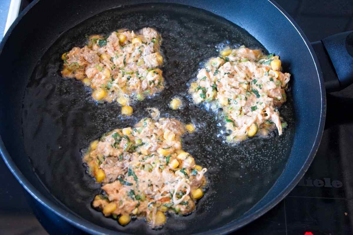Fritters frying in a shallow layer of oil in a pan, showing bubbling edges and lightly golden batter.