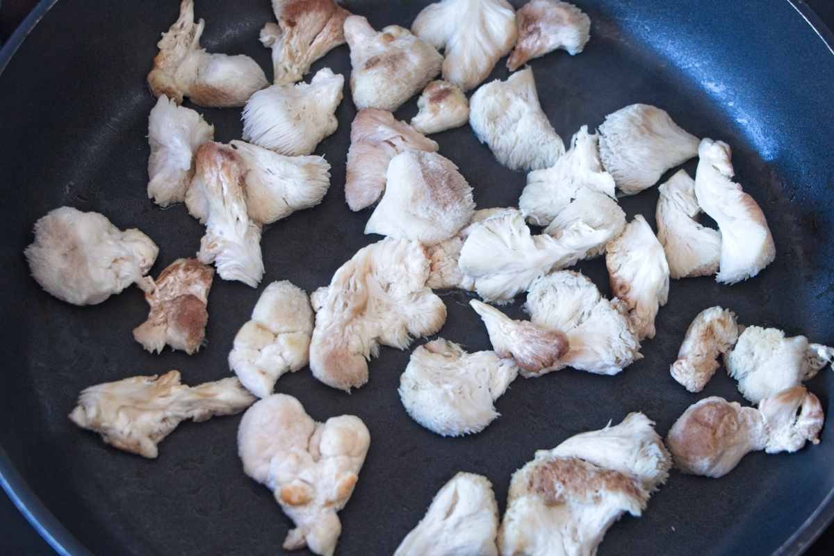 Torn pieces of lion’s mane mushroom cooking in a dry pan to release moisture before squeezing and chopping.