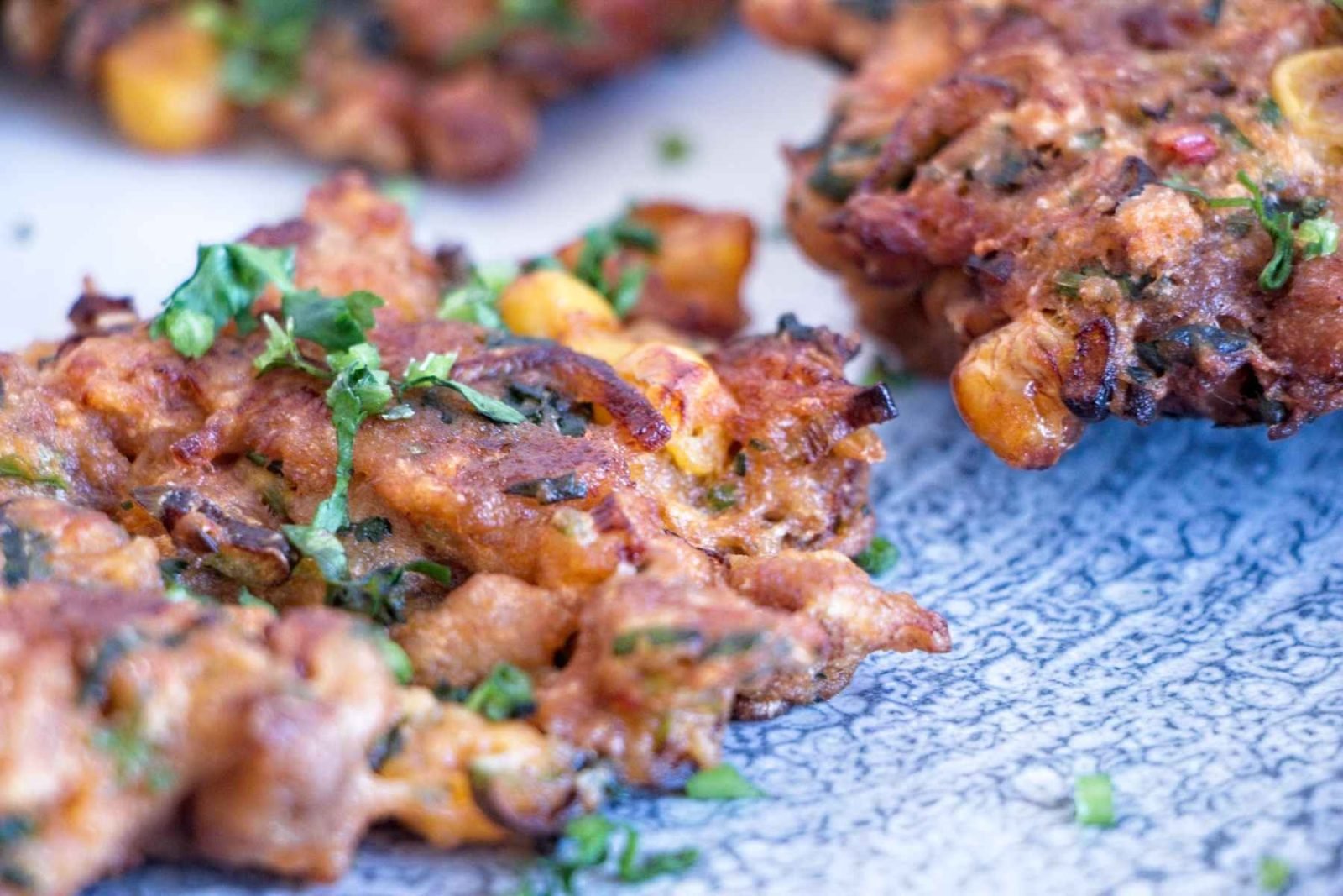 Close-up of crispy lion’s mane mushroom fritters showing golden edges, sweetcorn pieces, and chopped herbs on top.